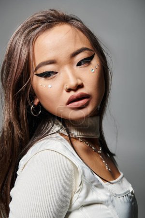 alluring asian young woman with heavy makeup looking to back against grey background