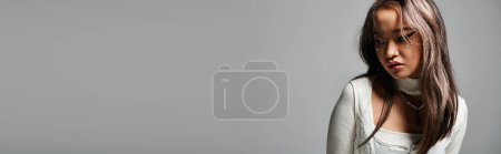 Téléchargez les photos : Bannière de jeune fille couvrant le visage avec des cheveux et regardant de côté sur fond gris - en image libre de droit