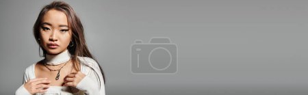 Téléchargez les photos : Bannière de jeune femme en tenue blanche avec un maquillage lourd et collier argenté sur fond gris - en image libre de droit