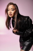 pretty woman in black leather outfit with heavy makeup sideways leaning forward on lilac background Poster #698336488