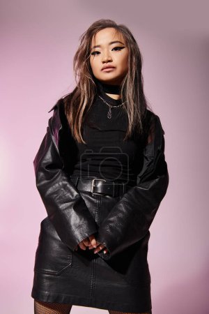 hermosa mujer joven asiática en traje de cuero negro posando sobre fondo lila