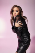 attractive asian woman in black leather outfit hug herself sideways on lilac background Poster #698337140