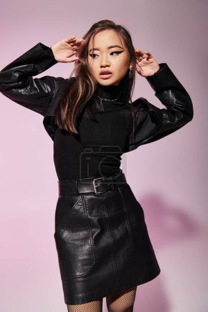 lovely asian woman in 20s in black leather outfit hold up hands around to face on grey background