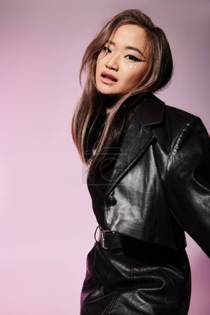 Téléchargez les photos : Charmante asiatique jeune fille en cuir noir tenue avec lourd maquillage debout latéralement - en image libre de droit
