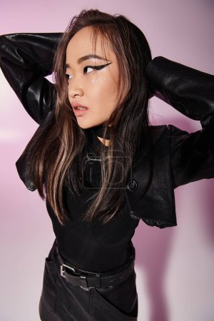 charming asian young woman in leather outfit putting hands behind head and looking to up