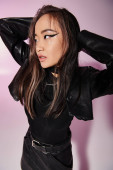 charming asian young woman in leather outfit putting hands behind head and looking to up Sweatshirt #698337522