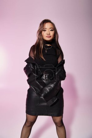 hübsche asiatische junge Frau im schwarzen Lederoutfit posiert vor fliederfarbenem Hintergrund