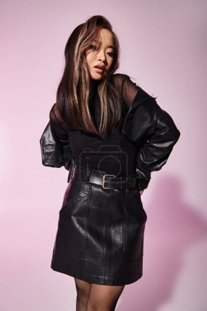 Charmante asiatische junge Frau in schwarzem Lederoutfit mit schwerem Make-up stehend und nach unten blickend