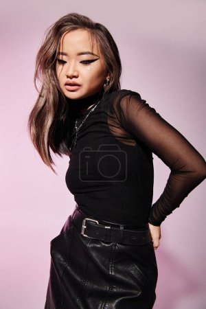 Téléchargez les photos : Charmante femme asiatique aux cheveux bruns et au maquillage lourd regardant vers le bas sur fond lilas - en image libre de droit