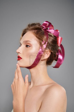 Eine junge Frau mit klassischer Schönheit posiert in einem Studio und strahlt Eleganz aus, während sie eine rosafarbene Schleife auf dem Kopf trägt.