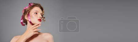 Téléchargez les photos : Une jeune femme respire la beauté classique, posant dans un studio avec un arc rose sur la tête sur un fond gris. - en image libre de droit