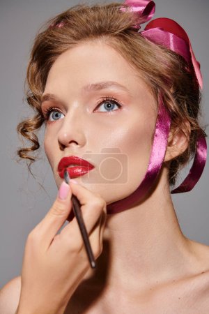Eine klassische Schönheit, eine junge Frau posiert elegant mit einer rosafarbenen Schleife auf dem Kopf in einem Studio vor grauem Hintergrund.