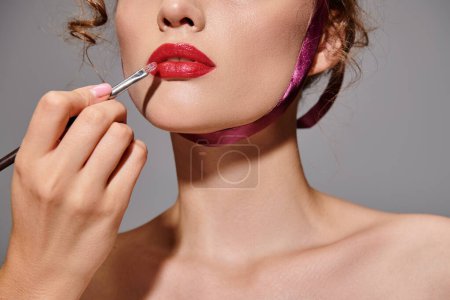 A young woman elegantly applying lipstick to her lips in a studio setting, showcasing classic beauty.