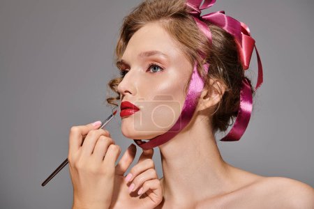Eine junge Frau mit klassischer Schönheit posiert in einem Studio-Setting und trägt eine rosa Schleife auf dem Kopf.