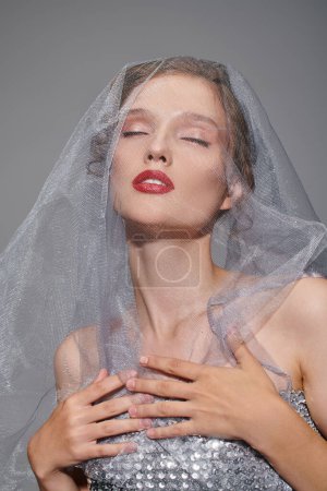 A young woman exudes classic beauty while posing in a studio, wearing a veil on her head.