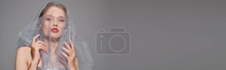 Téléchargez les photos : Une jeune femme respire la beauté classique en posant gracieusement avec un voile sur la tête dans un décor de studio sur un fond gris. - en image libre de droit