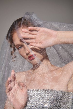 Eine junge Frau posiert in einem Atelier, gekleidet in ein Brautkleid mit einem Schleier, der anmutig über ihren Kopf fließt.