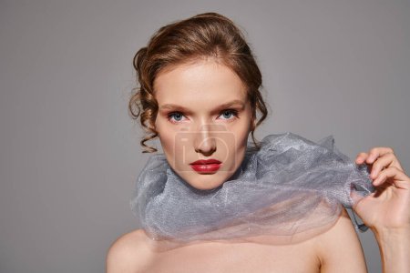 Une jeune femme respire la beauté classique dans un décor de studio, avec une écharpe élégante drapée autour du cou.