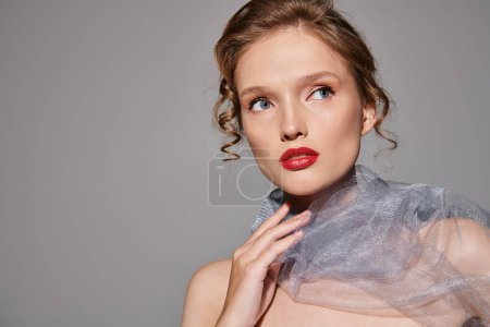 Une jeune femme respire la beauté classique en posant dans un studio, portant un voile et un rouge à lèvres rouge frappant.
