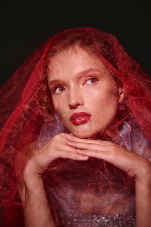 Eine junge Frau strahlt klassische Schönheit mit Schleier und fettem roten Lippenstift in einem Studio vor schwarzem Hintergrund aus.