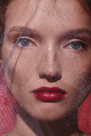 Eine atemberaubende junge Frau mit rotem Lippenstift posiert in einem Studio-Setting und präsentiert klassische Schönheit aus nächster Nähe.