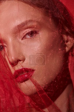 Une jeune femme aux cheveux roux éclatants et au rouge à lèvres assorti dégage une élégance intemporelle dans un décor studio sur fond noir.