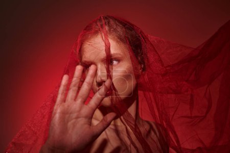 A young woman with classic beauty, covering her face with her hands in a studio setting against a black backdrop.