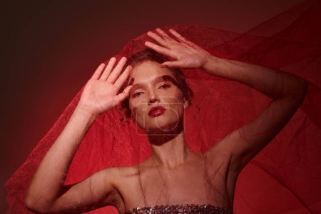 Foto de Una joven mujer exuda belleza clásica, vestida con un vestido rojo vibrante con sus manos elegantemente posicionadas en su cabeza. - Imagen libre de derechos