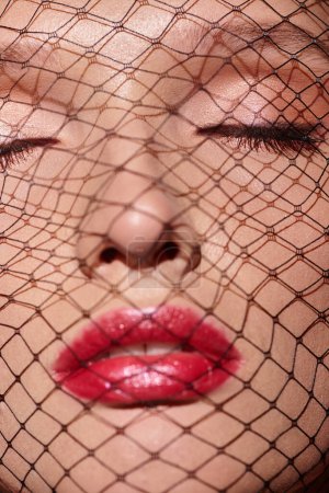 Eine klassische Schönheit mit rotem Lippenstift blickt durch ein Netz, das ihr Gesicht in einer mystischen und fesselnden Pose bedeckt.