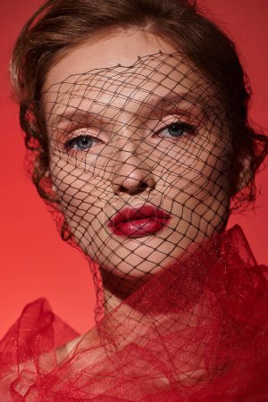 Eine junge Frau strahlt klassische Schönheit aus, als sie in einem Studio mit einem roten Schleier vor ihrem Gesicht posiert.