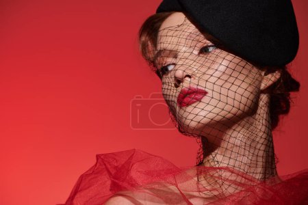 Téléchargez les photos : Une jeune femme respire la beauté classique, frappant une pose dans une robe rouge magnifique et un chapeau noir chic. - en image libre de droit