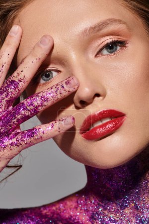 A young woman in a classic beauty pose, hands on her face covered in shimmering glitter, exuding elegance and charm.