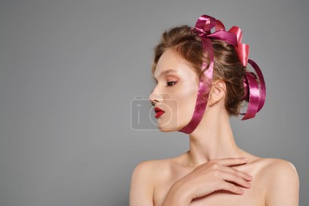 A young woman with classic beauty poses in a studio, her hair adorned with a delicate pink ribbon.