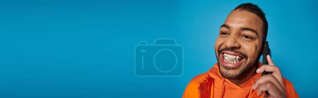 Photo for Banner of cheerful african american man calling in smartphone against blue background - Royalty Free Image