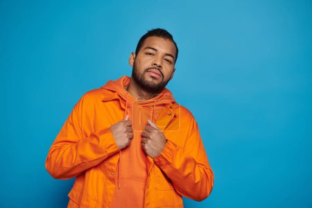 handsome african american young man in orange outfit posing against blue background