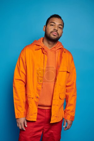 handsome african american young man in orange outfit standing against blue background