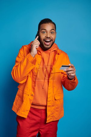 cheerful african american man calling in smartphone with credit card and surprised looking to camera
