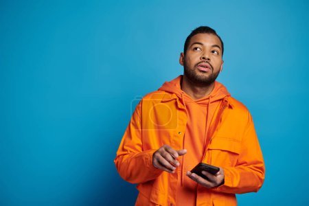 Téléchargez les photos : Bel homme afro-américain en tenue orange défilant dans les médias sociaux et regardant vers le haut - en image libre de droit