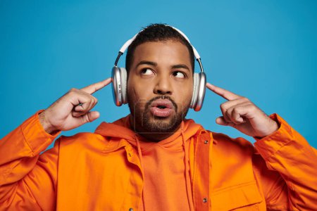 Téléchargez les photos : Attrayant jeune homme afro-américain regardant vers le haut et toucher les doigts pour écouteurs sur la tête - en image libre de droit