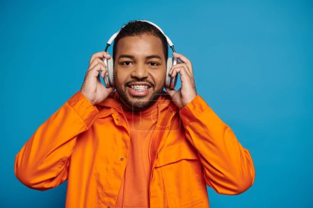 handsome african american man in orange outfit look to camera and hold with hands on headphones