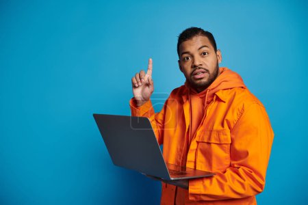 confused african american man in orange outfit with laptop came up with idea on blue background