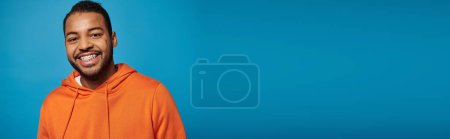 banner of cheerful african american man in orange outfit smiling broadly against blue background