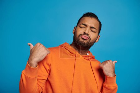 Photo for African american man with closed eyes outfit pointing away with thumbs on blue background - Royalty Free Image