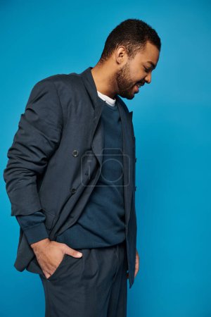 Afrikanisch-amerikanischer Mann im dunkelblauen Outfit steht zur Seite und schaut mit der Hand in der Tasche nach unten