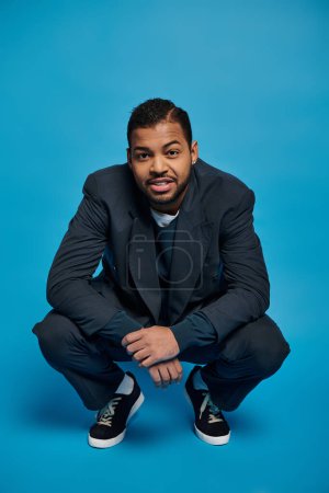 attractive african american man in dark blue outfit crouching down against vibrant background