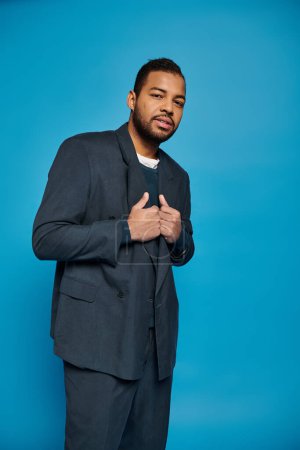 attrayant homme afro-américain en tenue bleu foncé posant sur le côté sur fond vibrant