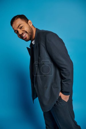 fröhlicher afrikanisch-amerikanischer junger Mann im dunkelblauen Outfit, der mit der Hand in der Tasche zur Seite steht