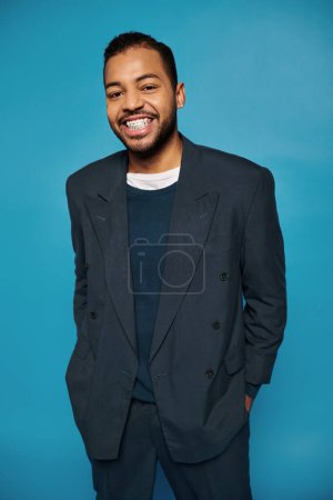 happy african american young guy in dark blue outfit smiling to camera with hands in pockets