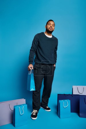 encantador hombre afroamericano en traje azul oscuro de pie con bolsas de compras y mano en el bolsillo