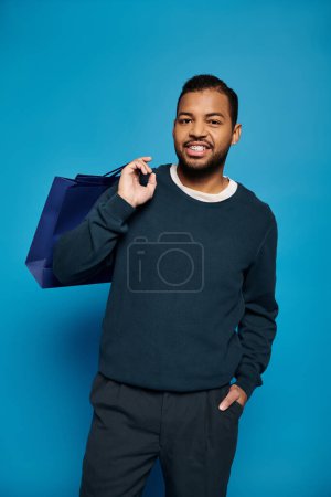 atractivo afroamericano joven con bolsa de compras sobre hombro y mano en bolsillo